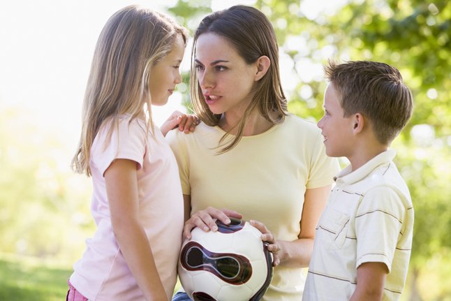 Woman and two young children outdoors holding volleyball and smi