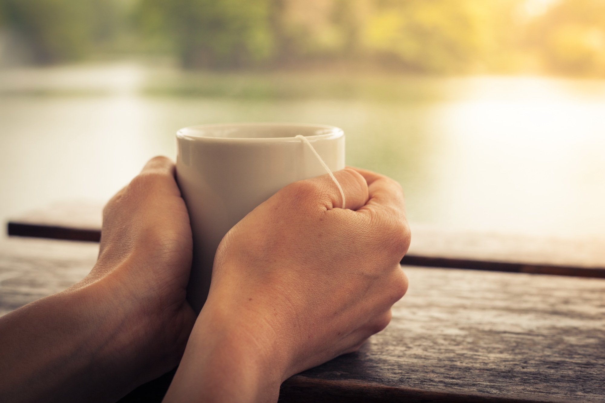 Closeup on a woman's hands holding a cup of tea by a lake in the afternoon