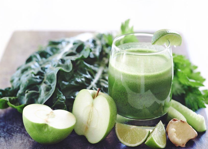 Juiced health juice in glass surrounded by cut up lime, ginger, apple, celery and spinach