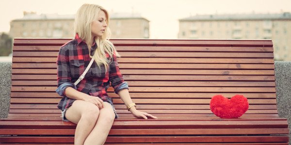 Sad lonely girl sitting on a bench near to a big red heart